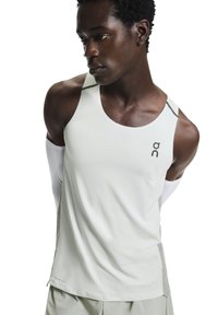 Débardeur de sport gris clair avec un col rond, un marquage minimaliste et des accents contrastants aux épaules. Le tissu semble lisse et respirant.