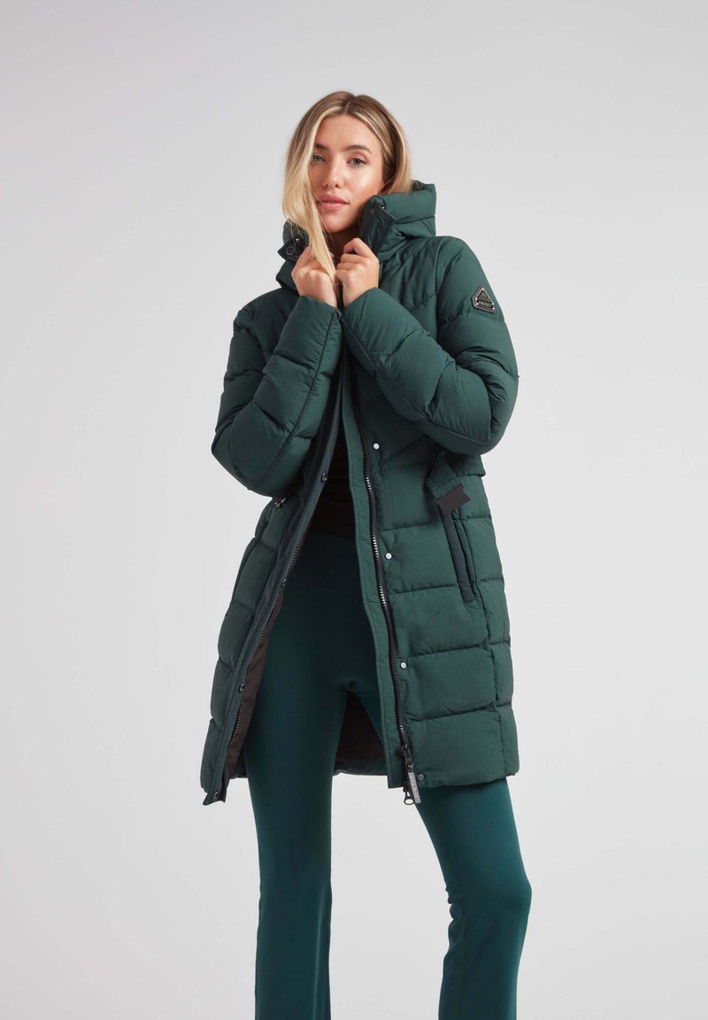 Chaqueta de plumas verde oscura con cuello alto, acolchado horizontal, cremallera frontal y botones a presión. Presenta un parche de logo en el hombro.