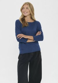 Bluză tricotată bleu marin, cu mânecă lungă, guler rotund și accente drepte, combinată cu pantaloni negri cu croi larg. Textură netedă, croi lejer.