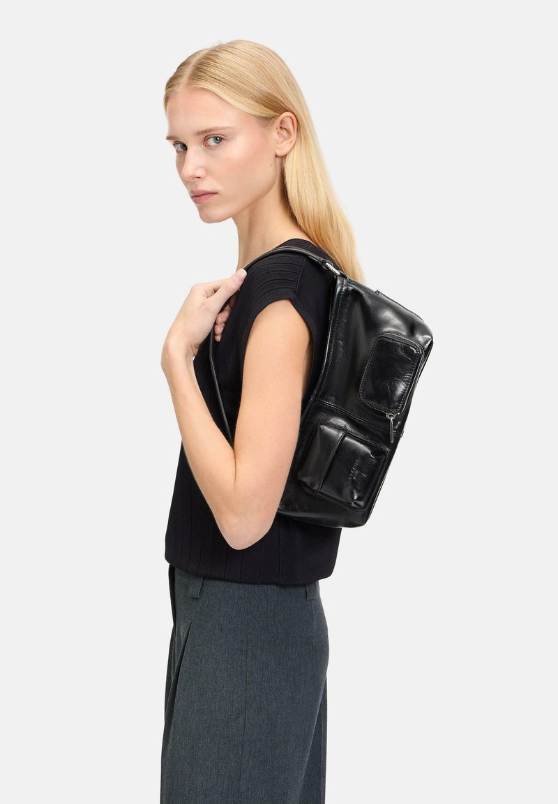Mochila de cuero negro con varios bolsillos, diseño elegante y textura pulida. Correas ajustables, forma cuadrada compacta y cierre de cremallera.