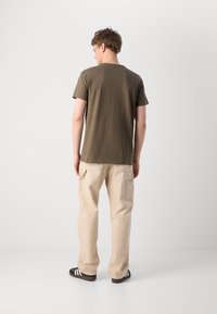 Olivengrønn t-skjorte, kortermet, rund hals, kombinert med beige cargo-bukser, med sidelommer, og svarte sandaler med hvite striper.