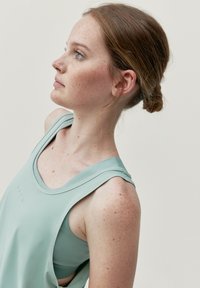 Světlý zelený sportovní top bez rukávů s kulatým výstřihem a širokými ramínky, vyrobený z texturované tkaniny a s volným střihem pro pohodlí.