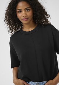 Black, short-sleeve top made of soft fabric. Features a rounded neckline and center seam detail. Worn with light denim.