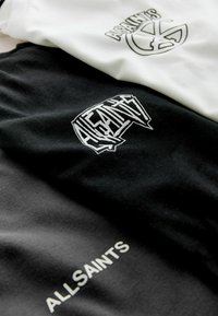 Trzy t-shirty: jeden czarny z białym logo graficznym i tekstem, jeden biały z czarnym logo graficznym. Materiał bawełniany, płaska tekstura, casualowy design.