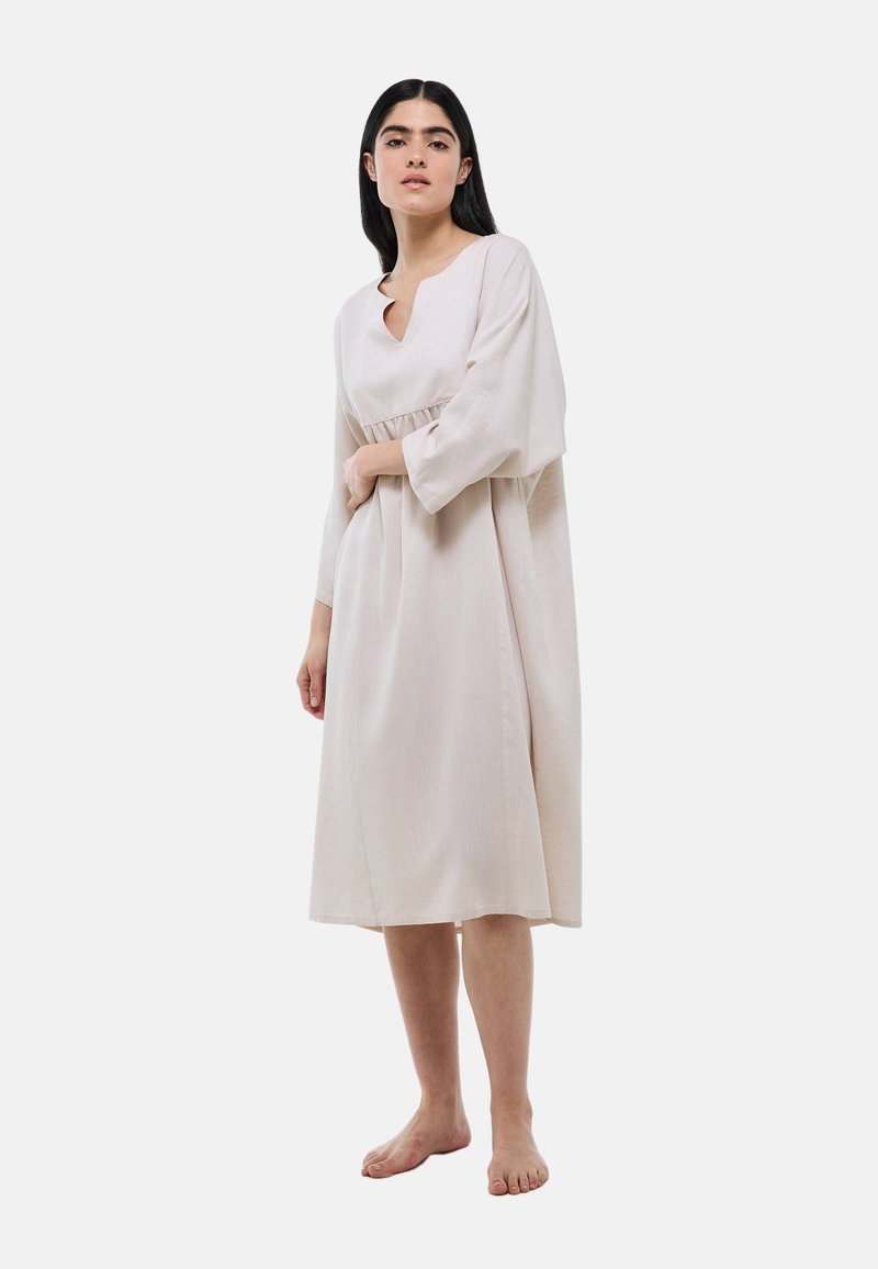 Robe en lin beige avec un col rond et un détail en forme de clé. Comprend des manches longues, une couture à la taille et tombe à mi-mollet.