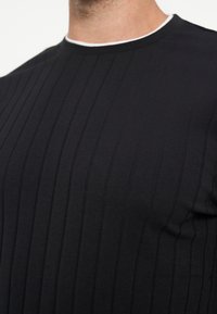 Κοντινό πλάνο ενός ατόμου που φοράει μαύρο ριμπ πουλόβερ με λευκή επένδυση γύρω από τον λαιμό.
