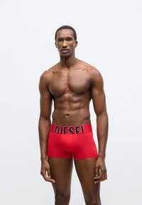 Červené bavlnené boxerky s čiernym pásom so značkou "DIESEL". Majú priliehavý strih a dĺžku do polovice stehna.