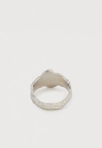 Srebrn prstan z organsko, neenakomerno teksturirano površino in subtilno valovito obliko, prikazan na enostavni beli podlagi.