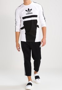 Dlouhý rukáv tričko Adidas s černobílými panely a logem. Kombinováno s černými tepláky s bílými bočními pruhy a pantoflemi.