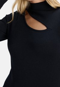 Maglione nero con collo alto e un dettaglio intagliato unico sul petto. Realizzato in un tessuto in maglia testurizzato, silhouette aderente.