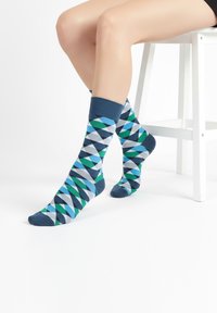 Calcetines coloridos con un patrón geométrico en tonos de azul, verde, gris y azul oscuro, con un puño acanalado en contraste.