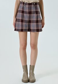 Gonna corta a quadri in tonalità bordeaux, blu e bianco, con vita alta, due tasche e silhouette aderente, abbinata a stivali alla caviglia beige.