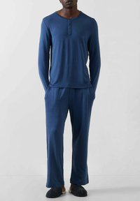 Marineblå langærmet top med henley-udskæring og tre knapper, kombineret med matchende løstsiddende bukser. Stoffet ser glat og blødt ud.