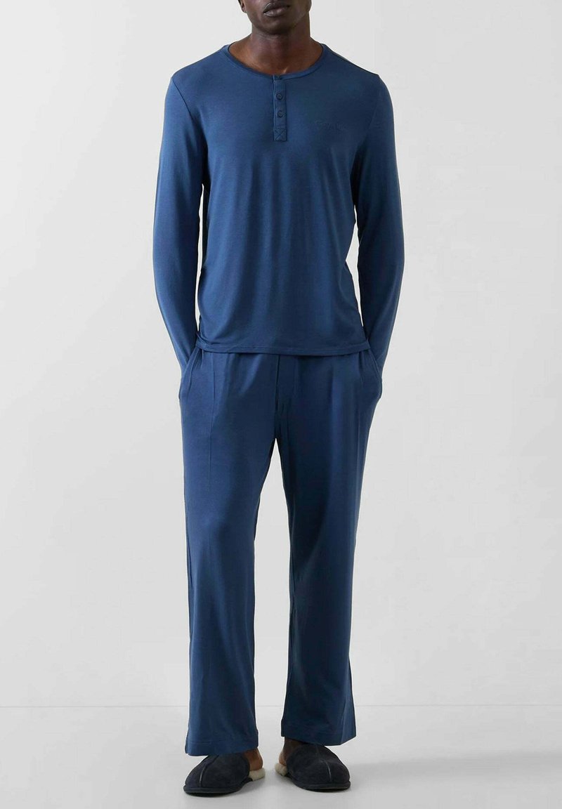 Marineblå langærmet top med henley-udskæring og tre knapper, kombineret med matchende løstsiddende bukser. Stoffet ser glat og blødt ud.