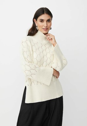 Pullover di maglia color crema con collo alto, caratterizzato da fantasie a foglia lavorate a giorno e maniche ampie. Il dettaglio dell'orlo spaccato aggiunge struttura.