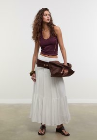 Burgundy crop-top, valkoinen kerroksellinen maxi-hame, ruskea vyölaukku ja ruskeat sandaalit. Teksturoitu kangas, rento muotoilu, kerrokselliset yksityiskohdat.