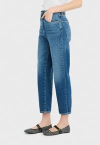 Jeans de tiro alto azul claro con corte recto, cinco bolsillos y un sutil desgastado. Combinados con zapatos planos de patrón en blanco y negro.