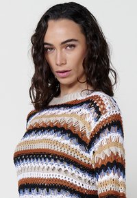 Multicolored knitted sweater featuring horizontal stripes in brown, blue, black, cream, and tan. Open weave design with a round neck.
