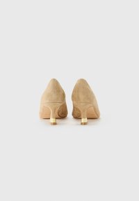 Beige suede kitten heel shoes with gold metallic accents on the heels, viewed from the back on a white background.