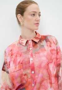 Camicia button-up in rosa e corallo con stampa floreale, dotata di colletto, una tasca singola e bottoni azzurri chiari sul davanti.