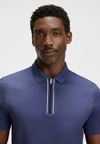 Granatowa koszulka polo z krótkim zamkiem błyskawicznym i białymi akcentami, z klasycznym kołnierzykiem i teksturowanym materiałem.