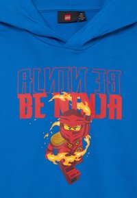 Hoodie in cotone blu con una grafica rossa di un ninja circondato da fiamme, accompagnata dal testo "BE NINJA" in grassetto rosso.