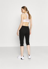 Sutiã desportivo branco com design de costas nadador e calças capri atléticas pretas com cintura ajustada e punhos. Modelo a usar ténis brancos.