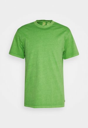 Zaļš kokvilnas T-krekls ar apaļu kaklu un īsām piedurknēm. Mīksta tekstūra un nedaudz izbalējusi izskats. Nav redzamu logo vai rakstu.