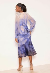 Langærmet, let kjole med blå og lilla blomsterprint, transparent tekstur og flæsekantede manchetter, kombineret med sølvfarvede sandaler med stropper.