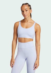 Sostén deportivo de color púrpura claro con un diseño simple y tirantes ajustables, combinado con mallas de tiro alto en púrpura claro, con textura suave.