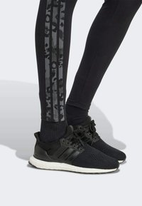 Black athletic shoes with textured mesh upper, three stripe accents, and white sole. Black leggings with gray leopard print side stripes.