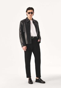 Must nahktagi, valge t-särk, mustad püksid ja mustad tossud. Päikeseprillid rõhutavad välimust. Sujuv tekstuur ja kaasaegne disain.