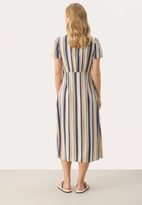 Robe rayée avec des manches courtes, un corsage ajusté et une jupe évasée. Les couleurs incluent le marine, la crème et des teintes pastel. Portée avec des sandales plates.