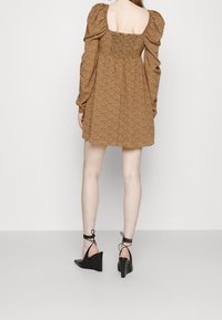 Mini-robe marron à motifs avec manches bouffantes et détail dos smocké. Associée à des sandales compensées à lanière cheville noires.