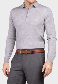 Grauem Langarm-Polo mit Kragen, zwei Knöpfen und einer subtilen Textur, kombiniert mit grauen Hosen und einem braunen Ledergürtel.