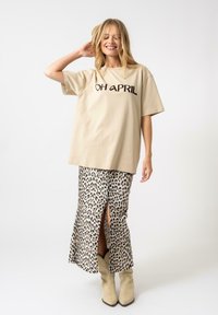 Camiseta oversized beige con el texto "OH ABRIL" combinada con una falda de estampado de leopardo con una abertura frontal, llevada con botas de tobillo beige.