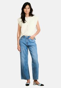 Adīta krēmkrāsas bezpaliktņa blūze ar apaļu izgriezumu un pogām, apvienota ar gaiši zilo platā kāju džinsu un divkrāsu plakanām kurpēm.