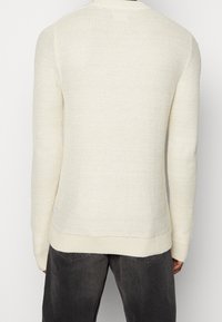 Krémový pletený svetr s texturovaným vzorem, kulatým výstřihem a žebrovanými manžetami. Zobrazen zezadu, s mírně volným střihem.