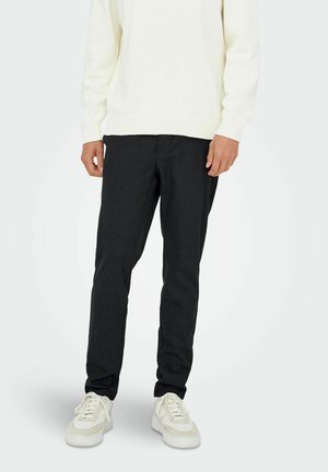 Schwarze, taillierte Hose aus strukturiertem Stoff mit regulärer Passform und Seitentaschen, kombiniert mit einem hellen Strickpullover und Sneakers.
