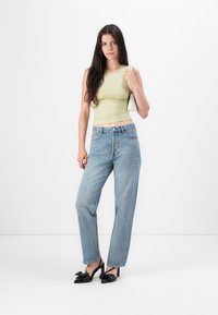 Débardeur ajusté vert clair, jeans droits taille haute bleu clair, et escarpins noirs avec des nœuds. Modèle tenant un petit sac blanc.