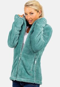 Giacca in pile teal fuzzy con zip completa, tasche laterali e tessuto testurizzato. Presenta una vestibilità rilassata e un orlo arrotondato. Finitura morbida al tatto.