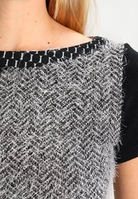 Maglione bianco e nero con una texture fibrosa e lunga sulla parte anteriore e un retro e maniche lisce e di un nero uniforme. Collo rotondo con dettagli.