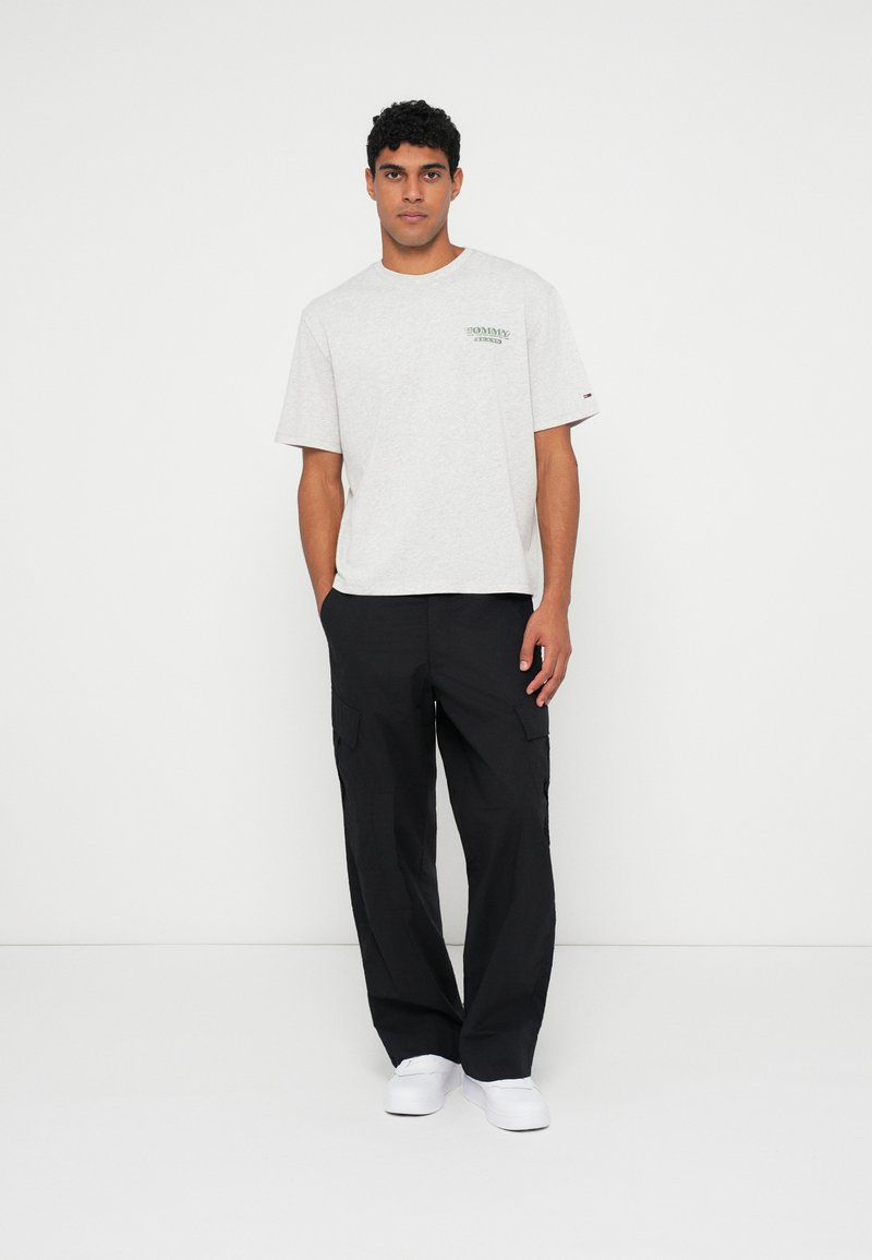 Grå bomulls t-skjorte med grønn logo på brystet, kombinert med svarte cargo-bukser med side lommer og hvite slip-on sko.