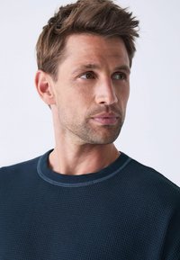 Mørkeblå strikket sweater med rund hals og kontrasterende syninger. Har korte ærmer og en afslappet pasform.