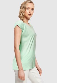 Minti vihreä lyhythihainen T-paita V-päällä ja rentoa tyyliä, valmistettu pehmeästä puuvillasekoitekankaasta, yhdistetty valkoisiin housuihin.