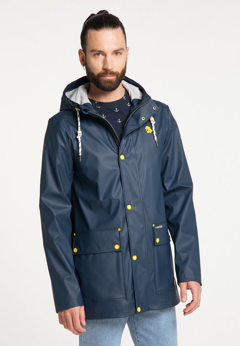 Marineblaue wasserdichte Jacke mit grauem Innenfutter, gelben Knöpfen und Kordelzugkapuze. Sie hat zwei Fronttaschen und einen Reißverschluss.