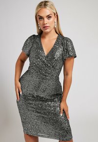 Musta paljettimekko, jossa on V-pääntie, lyhyet puffihihat, kapea siluetti, polvipituinen helma ja tekstuurihohde.