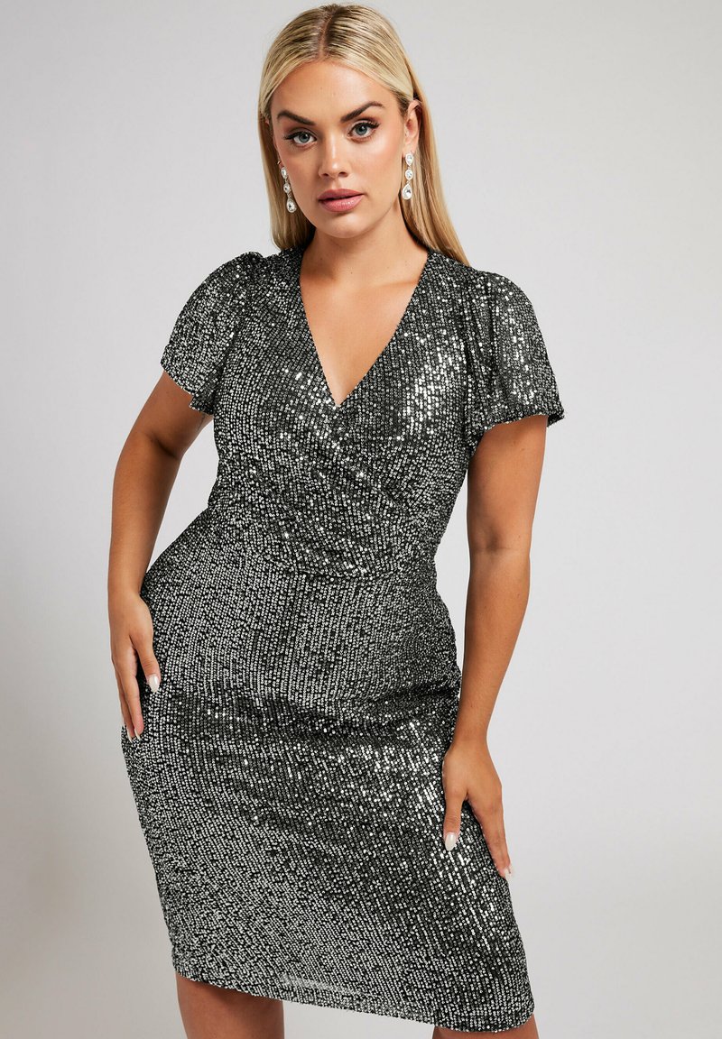 Musta paljettimekko, jossa on V-pääntie, lyhyet puffihihat, kapea siluetti, polvipituinen helma ja tekstuurihohde.