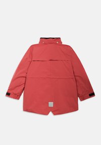 Raudona atspari vandeniui striukė su aukštu apykakle, spaustuko užsegimu ir juodomis detalėmis ant rankogalių. Yra atvira nugaros ventiliacija ir ženklas prie hem.