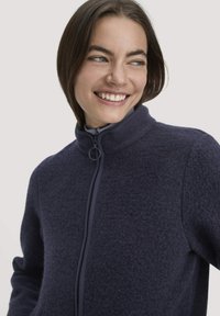 Marine fleecejack met hoge kraag en volledige rits. Textuurstof; ronde ritsen trekker; minimalistisch ontwerp.